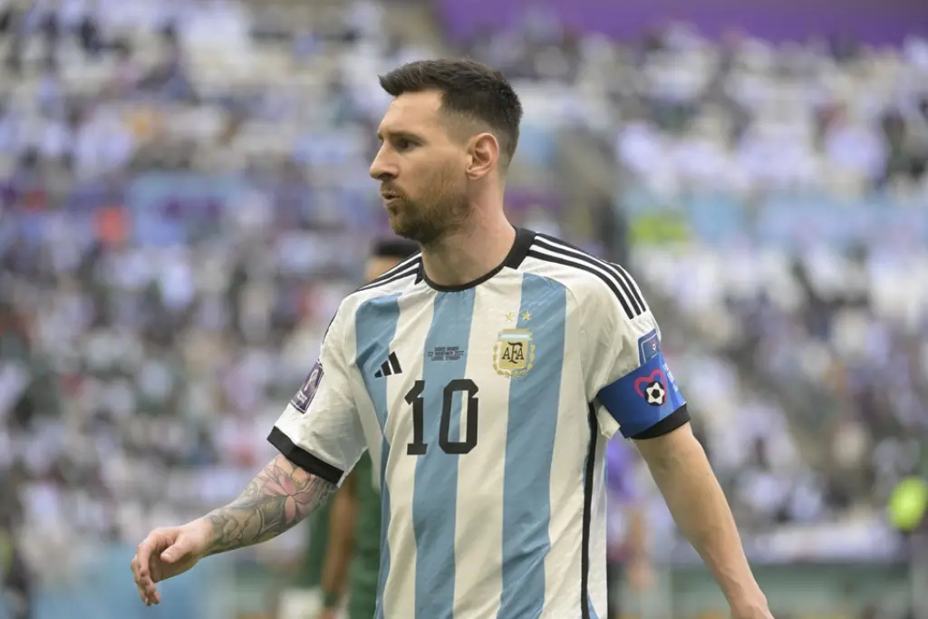 Close do jogador Lionel Messi usando a braçadeira de capitão da Argentina durante uma partida, ele que ocupa o topo da lista de jogadores com mais jogos na história da Copa do Mundo.