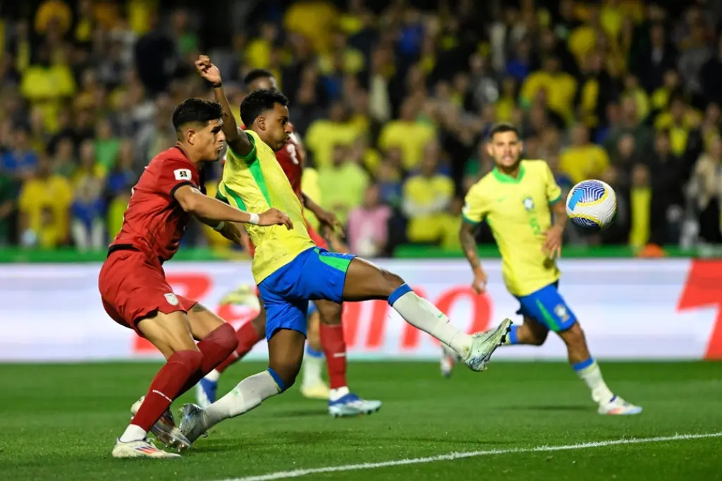 O jogador Rodrygo disputa a posse de bola com um adversário durante um jogo do Brasil. A imagem captura a intensidade da competição que define a posição das seleções na tabela das eliminatórias da copa do mundo 2026.