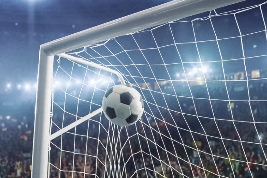 Close lateral de uma bola de futebol estufando a rede no ângulo superior do gol em um estádio lotado à noite, ilustrando o marco de quem fez o primeiro gol na história das copas do mundo fifa de futebol masculino.