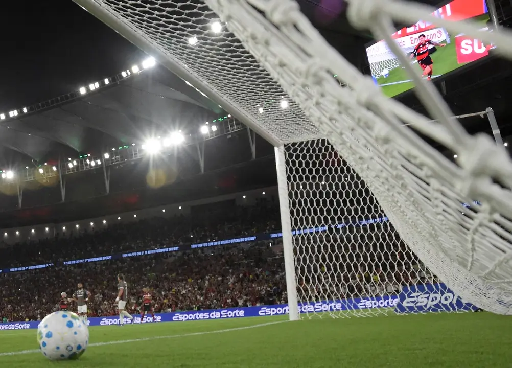 Vista de dentro da rede do gol durante partida entre Flamengo e Fluminense no Maracanã, pelo Campeonato Brasileiro, com torcida ao fundo e bola próxima à linha do gol. A imagem ilustra o tema “como apostar no campeonato brasileiro”