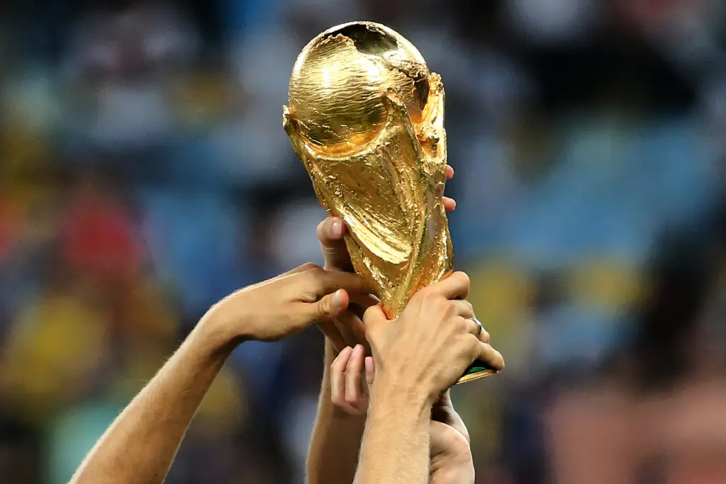 Taça da Copa do Mundo da FIFA sendo erguida por várias mãos em um estádio, com fundo desfocado e iluminação destacando o troféu dourado. A imagem representa o sonho dos convocados do Brasil para a Copa do Mundo 2026 em busca do hexacampeonato.