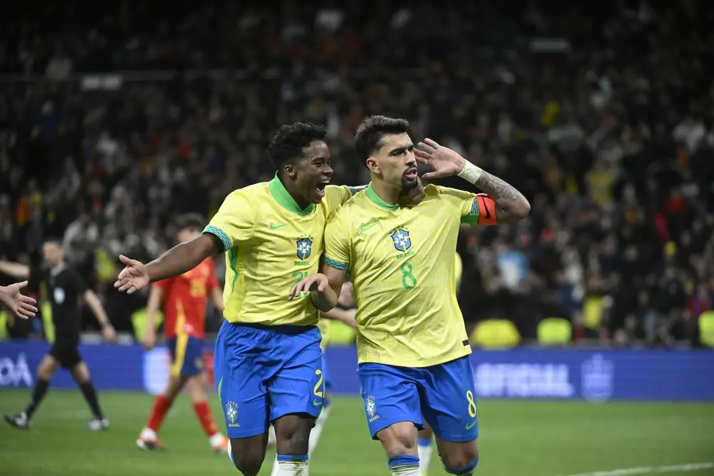 Jogadores da Seleção Brasileira comemoram durante partida internacional, com um atleta fazendo gesto para a torcida em estádio lotado. A imagem ilustra os convocados do Brasil para a Copa do Mundo 2026 em clima de celebração e expectativa pelo torneio.