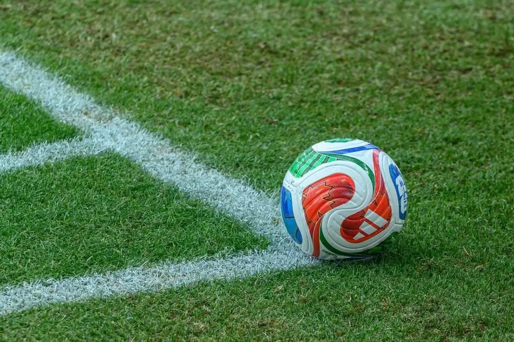 Previsões para copa do mundo 2026 representadas por uma bola oficial posicionada próxima à linha de escanteio em um gramado de estádio, destacando o clima de competição, expectativa e análises sobre as seleções que disputarão o torneio mundial.