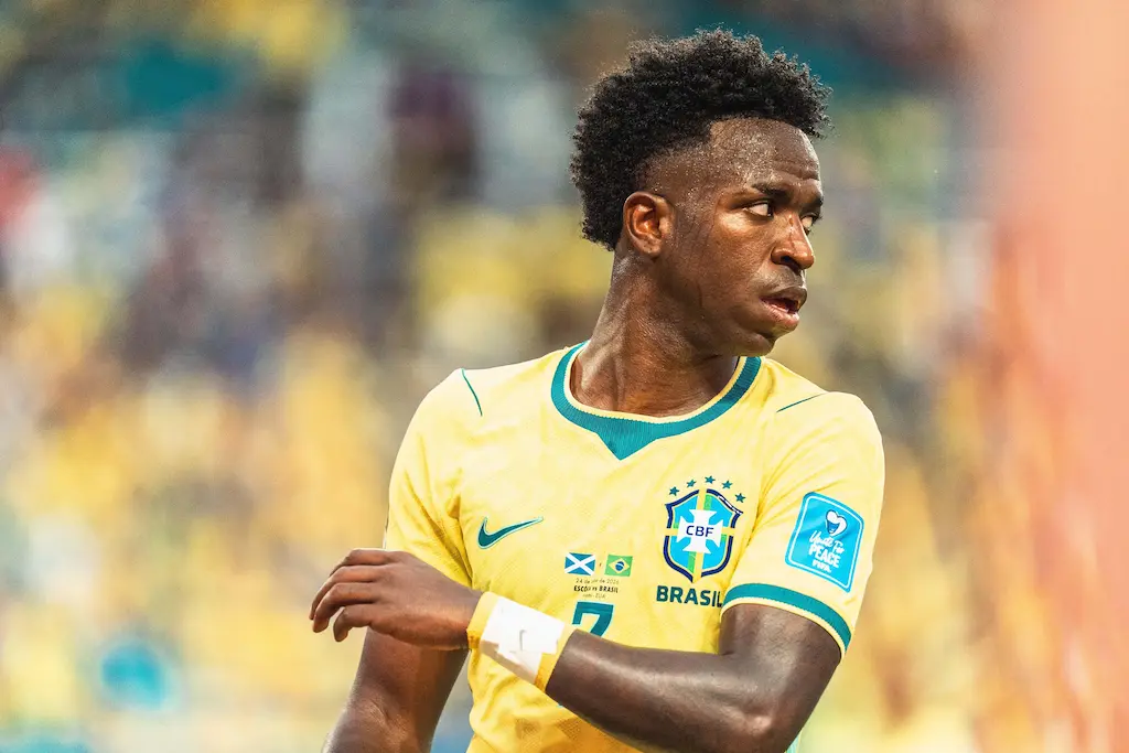Vinicius Jr., da seleção brasileira em campo usando camisa amarela do Brasil, com estádio desfocado ao fundo.